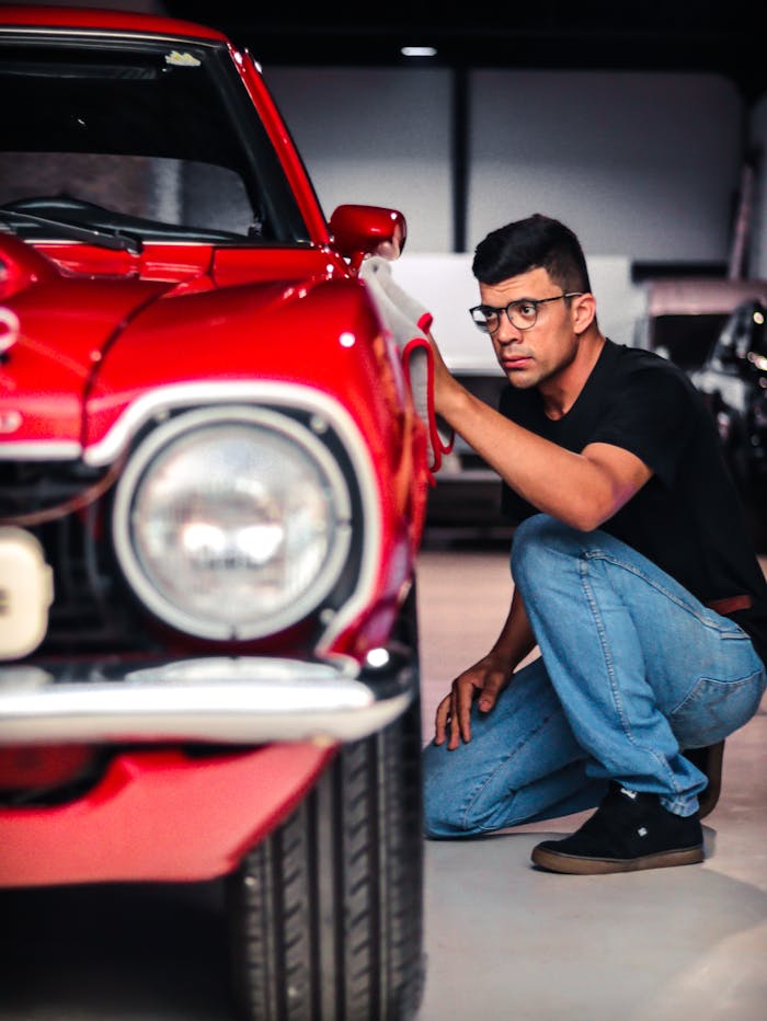 services-02 A man kneels to inspect a classic red car in a garage setting, emphasizing detail and care.